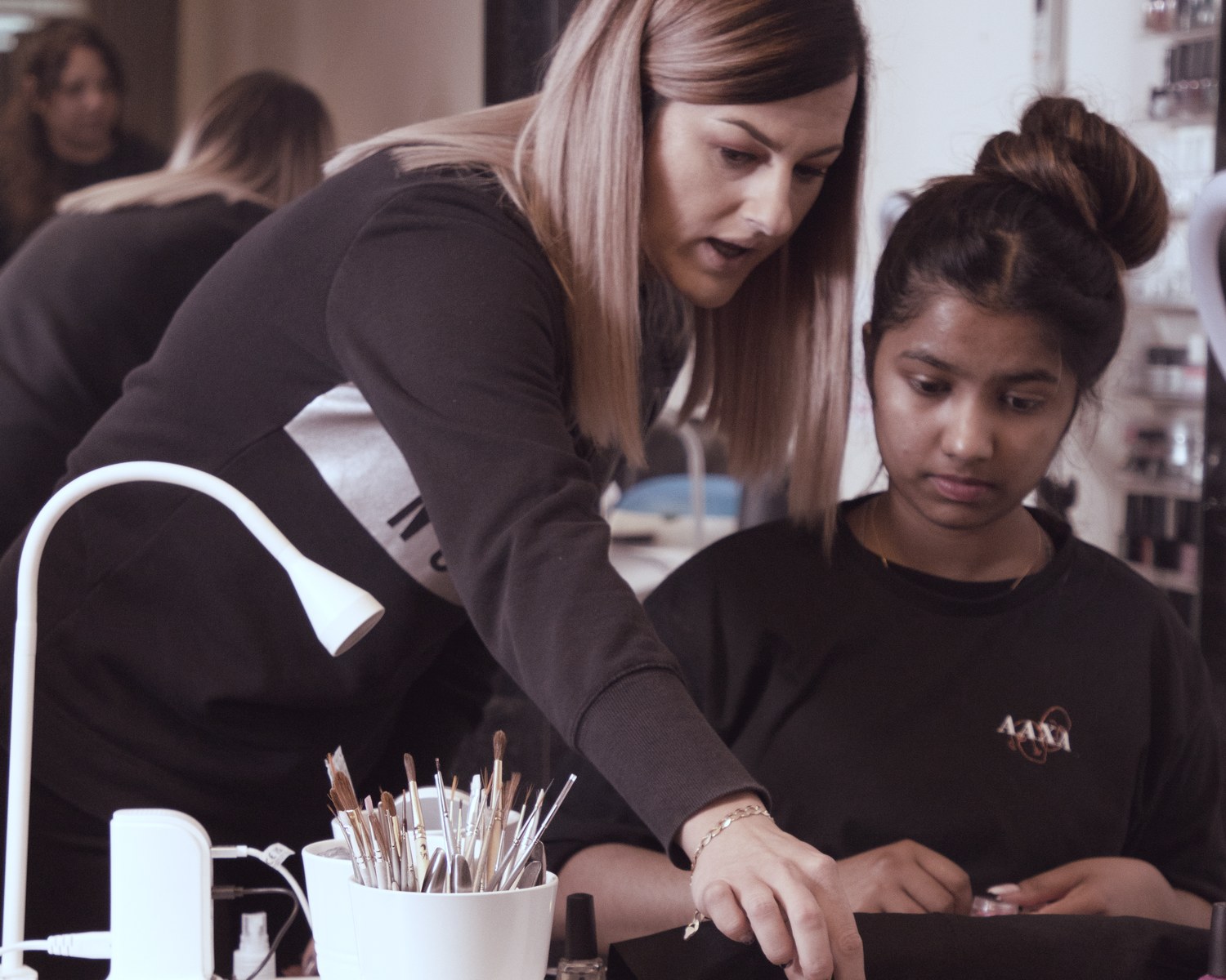 An AAXA tutor guiding a learner through nail art at a training station