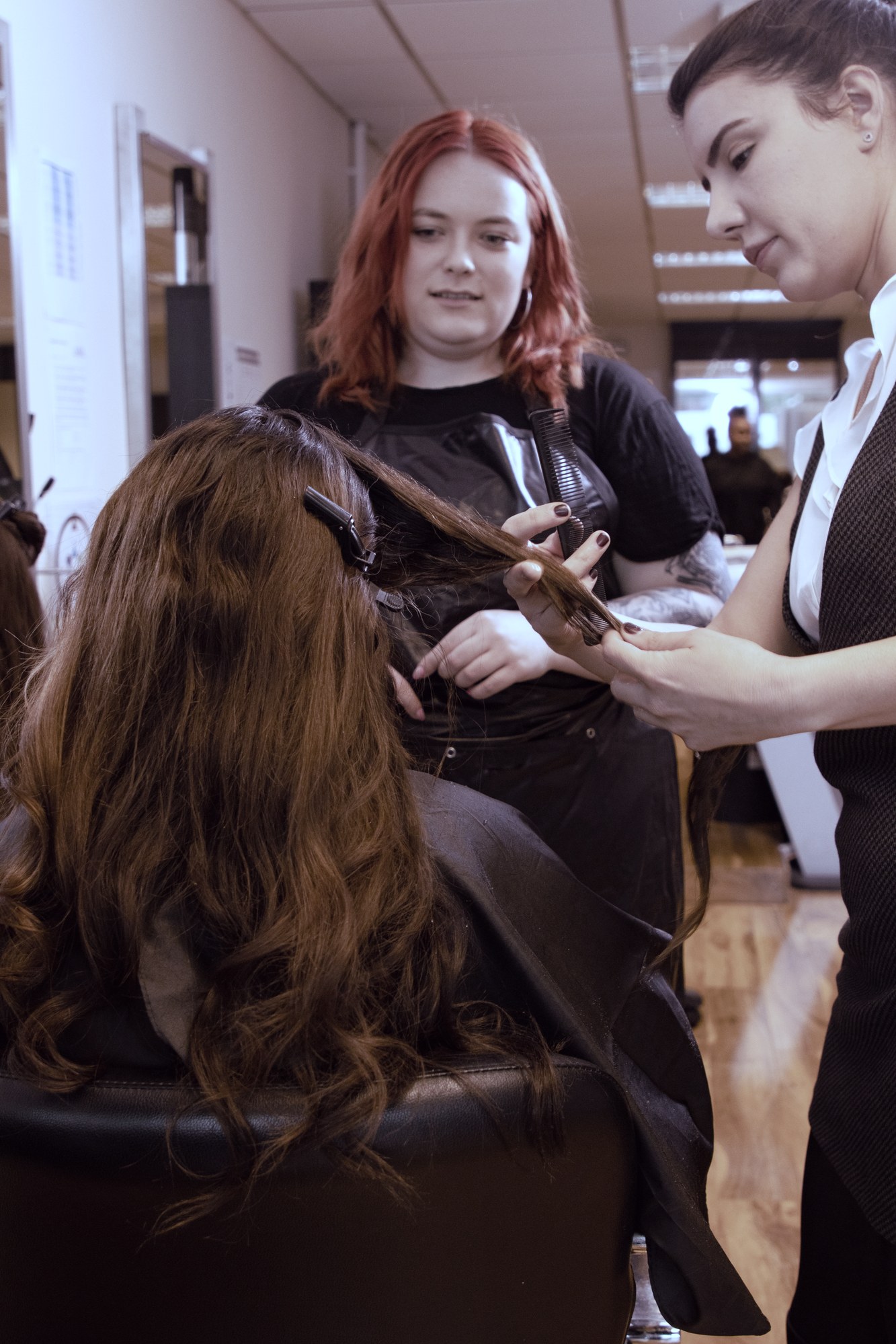 A hairdressing apprentice working on a client's hair with her trainer in the salon
